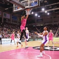Telekom Baskets Bonn Spieler in pinken Trikots dominieren ein Basketballspiel in einer großen, voll besetzten Arena.Players in pink jerseys dominate a basketball game in a large, packed arena.