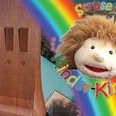 Kinder-Kirche Buntes Kinderkirche-Logo mit Regenbogen und fröhlicher Puppenfigur auf Kirchturmhintergrund.