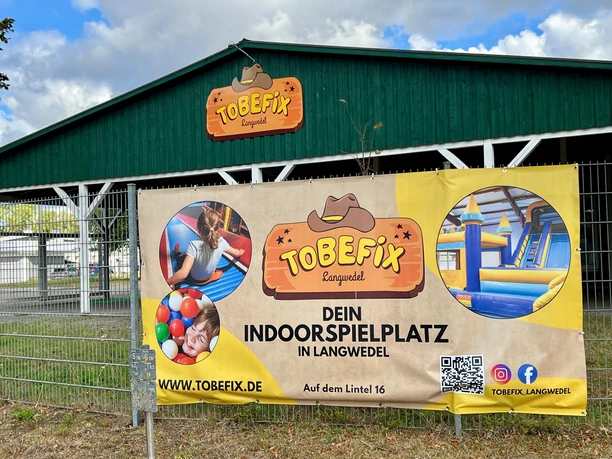 A large green shed with the Tobefix logo and a banner advertising an indoor playground in Langwedel.