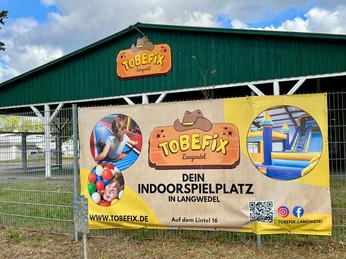 Tobefix Ein großer grüner Schuppen mit Tobefix-Logo und Banner, das einen Indoorspielplatz in Langwedel bewirbt.