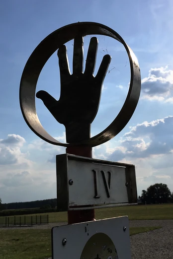 Römerlager Delbrück-Anreppen Skulptur einer Hand in einem Kreis vor einem weiten Feld, Wolken und blauem Himmel im Hintergrund.