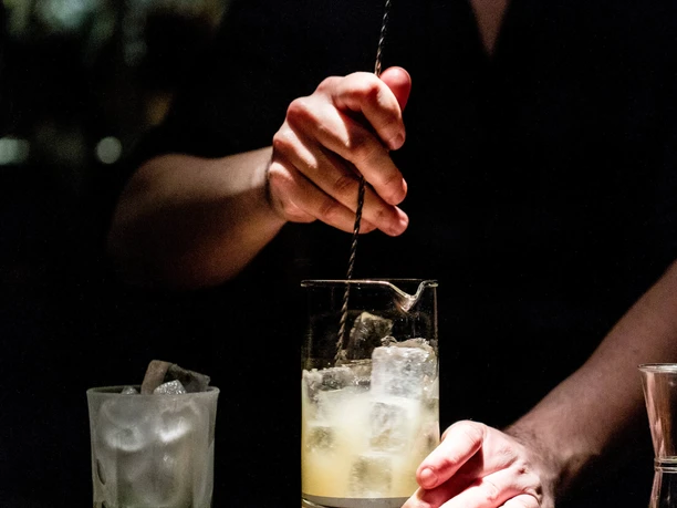 Suderman A bartender concentrates on mixing a cocktail while another cocktail glass is ready.