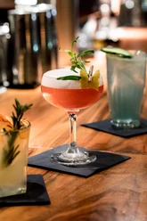 Suderman Ein Cocktailglas mit roter Flüssigkeit und Schaumkrone steht auf einem Holztresen.