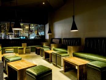 Suderman Ein modernes Café-Interieur mit hölzernen Tischen, grünen Sitzbänken und gedimmter Beleuchtung.A modern café interior with wooden tables, green benches and dimmed lighting.