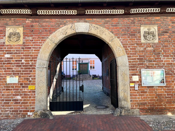 A stone archway leads into a paved courtyard; a historic building in the background.
