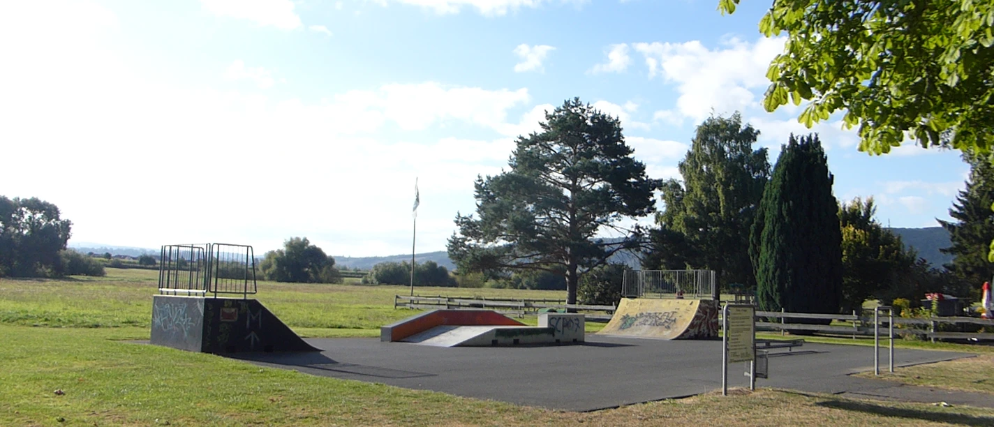 Asphaltierte Skatefläche mit mehreren Rampen auf einer Wiesenfläche.