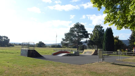 Skaterbahn Beverungen Asphaltierte Skatefläche mit mehreren Rampen auf einer Wiesenfläche.