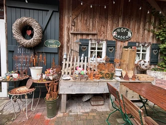 Der Hofladen ist hübsch gestaltet..JPEG Holzfassade mit liebevoll arrangierten Dekoartikeln, Pflanzen, Metallschmuck und Schildern eines Hofladens.
