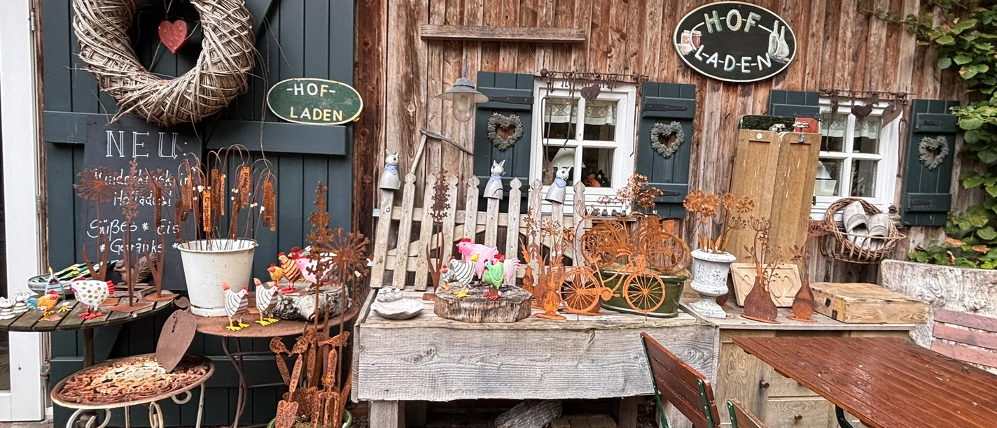 Der Hofladen ist hübsch gestaltet..JPEG Holzfassade mit liebevoll arrangierten Dekoartikeln, Pflanzen, Metallschmuck und Schildern eines Hofladens.