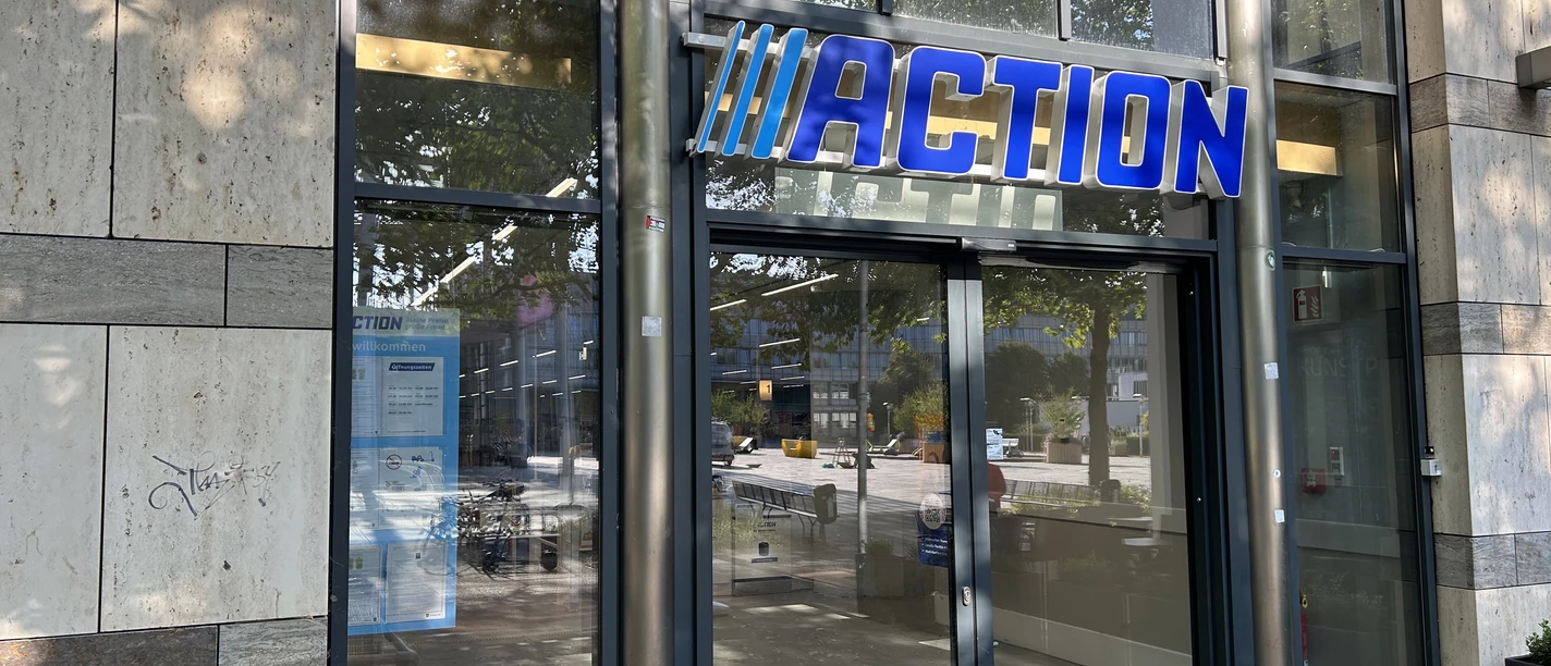 Action Eingang einer Action-Filiale mit großem blauen Markenlogo über den gläsernen Schiebetüren.