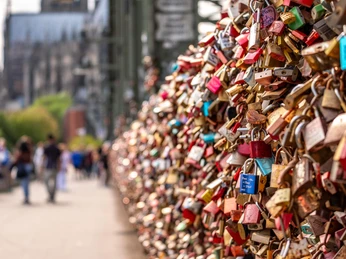 Love locks in Cologne Eine Vielzahl von bunten Liebesschlössern ziert das Geländer der Hohenzollernbrücke in Köln. Im Hintergrund verschwimmt die Silhouette des majestätischen Kölner Doms, ergänzt durch die vorbeiziehenden Menschen auf der Brücke, die zu Fuß den Rhein überqueren.A multitude of colorful love locks adorn the railing of the Hohenzollern Bridge in Cologne. The silhouette of the majestic Cologne Cathedral blurs in the background, complemented by the people passing by on the bridge as they cross the Rhine on foot.