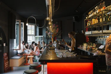 OFF Bar Eine bunt beleuchtete Bar mit Gästen, die an Tischen plaudern und Drinks genießen.