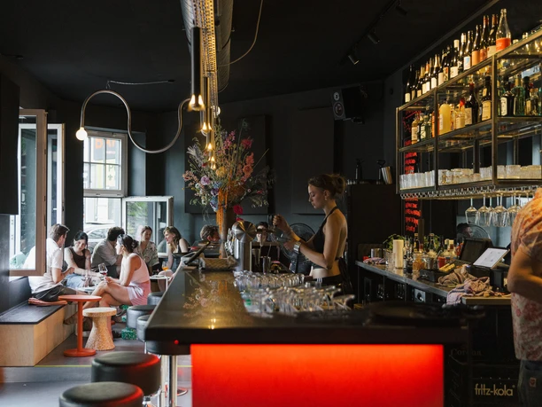 OFF Bar Eine bunt beleuchtete Bar mit Gästen, die an Tischen plaudern und Drinks genießen.
