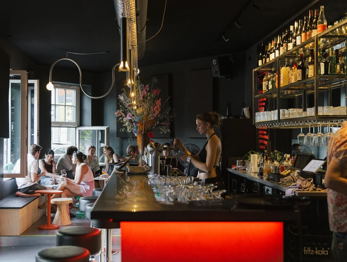 OFF Bar Eine bunt beleuchtete Bar mit Gästen, die an Tischen plaudern und Drinks genießen.A colorfully lit bar with guests chatting at tables and enjoying drinks.