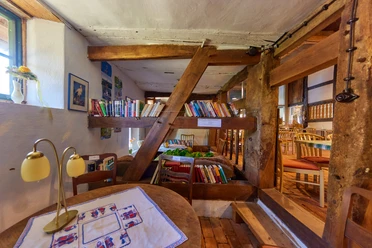 Ein rustikaler Innenraum mit Holzbalken, einer kleinen Bibliothek und gemütlichen Sitzplätzen.