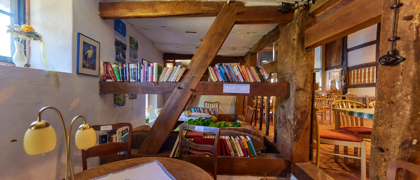 Ein rustikaler Innenraum mit Holzbalken, einer kleinen Bibliothek und gemütlichen Sitzplätzen.