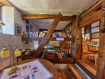 Blick in die Deele | Historische Hofstelle Windheim No2 im Mühlenkreis Minden-Lübbecke Ein rustikaler Innenraum mit Holzbalken, einer kleinen Bibliothek und gemütlichen Sitzplätzen.