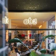 Oté Das Bild zeigt die helle und einladende Eingangsfassade eines Cafés oder Restaurants mit großen Glasfenstern und stilvoller Inneneinrichtung.