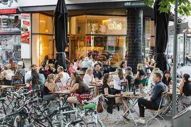 Oté A crowd enjoys drinks outside a café with large windows in Cologne.