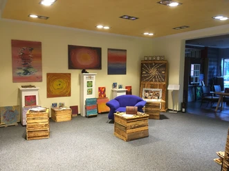 Kunstgalerie mit bunten abstrakten Gemälden an cremefarbenen Wänden und blauen Sesseln im Raum.