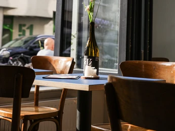 Frohnatur Bistrooo & Bar Bar Bar Das Bild zeigt den Innenbereich eines Cafés oder Restaurants mit Holzmöbeln und einer Blumenvase.The picture shows the interior of a café or restaurant with wooden furniture and a vase of flowers.