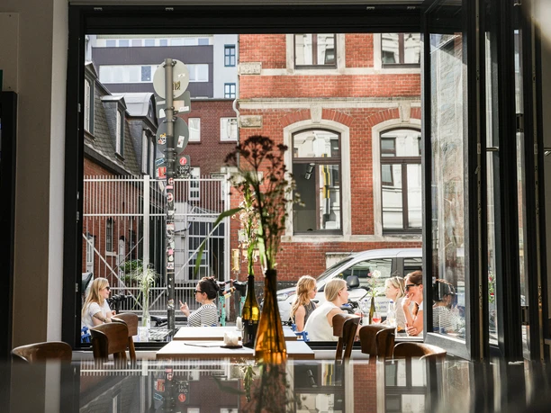 Frohnatur Bistrooo & Bar Bar Bar The picture shows a busy bar in an urban environment, photographed through an open window.