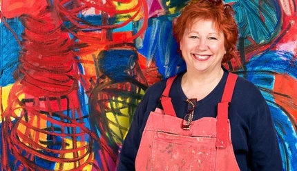 Künstlerin Barbara Salesch mag kräftige Farben Barbara Salesch steht lächelnd vor einem gemälde mit intensiven Rot- und Blautönen und trägt eine rote Schürze.