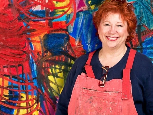 Künstlerin Barbara Salesch mag kräftige Farben Barbara Salesch steht lächelnd vor einem gemälde mit intensiven Rot- und Blautönen und trägt eine rote Schürze.