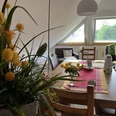 Essecke der Ferienwohnung Naturblick Das Bild zeigt ein Wohnzimmer mit einem großen Esstisch und dekorativen Blumen auf einem Tischläufer.