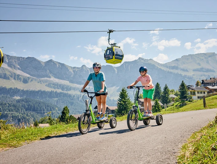 Bikeboard-Stockhütte (5).jpg Zwei Mädchen am Bikeboard fahren auf der Stockhütte.
