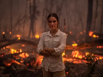 Grad jetzt - Against fear with Louisa Schneider Vor einem lodernden Flammenmeer steht Louisa Schneider in entschlossener Pose, die Arme verschränkt.Louisa Schneider stands in front of a blazing sea of flames in a determined pose, her arms crossed.