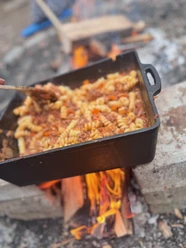 Fertiges Gericht am offenen Feuer_Markus Koch.jpg Nudeln mit Sauce in gusseiserner Pfanne über offenem Holzfeuer zubereitet