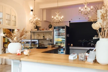 Das Neandertal No. 1 - Café und Events in Erkrath Ein helles Café mit Kronleuchtern, Holztresen und Kühlvitrinen, das eine warme Atmosphäre ausstrahlt.