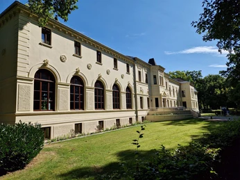 Altes-Kurhaus-Front.jpg Die Fassade des historischen Alten Kurhauses in Bad Zwischenahn unter klarem, blauem Himmel.