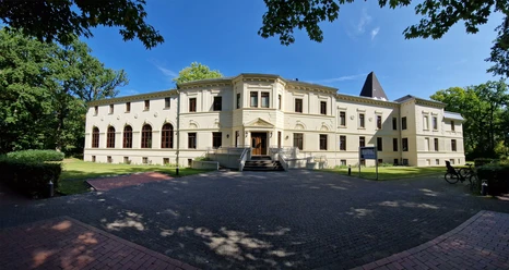 Altes-Kurhaus-Panorama.jpg Altes Kurhaus mit großen Fenstern, umgeben von Bäumen, in Bad Zwischenahn unter blauem Himmel.
