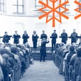 Musica Sacra Ukraina Das Bild zeigt ein Ensemble, das auf einer erhöhten Bühne im Inneren einer Kirche auftritt. Vor ihnen sitzt ein gefülltes Publikum, während ein Dirigent das Ensemble anleitet. Die Atmosphäre wirkt feierlich und konzentriert.The picture shows an ensemble performing on a raised stage inside a church. A full audience sits in front of them while a conductor leads the ensemble. The atmosphere is solemn and concentrated.