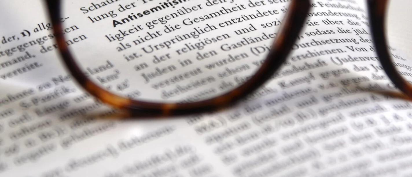 Verschriftlichte_Definition__Antisemitismus_.JPG Brille fokussiert den Lexikonbegriff Antisemitismus auf einer aufgeschlagenen Seite.