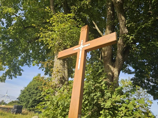 Bültekreuz aus Holz vor Bäumen und blauem Himmel in Pömbsen.