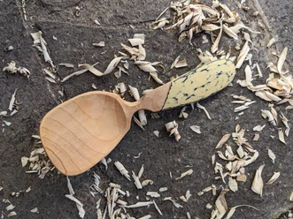 Halbfertiger Holzlöffel auf Steinboden umgeben von frischen Holzspänen