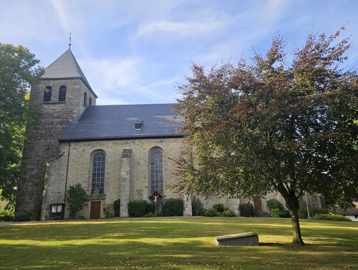 Mariä Himmelfahrt Kirche mit Turm, Wiese und Schatten eines Baumes im Vordergrund.
