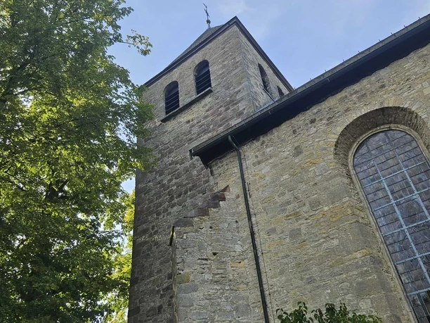Der Turm der Mariä Himmelfahrt Kirche Pömbsen steht zwischen Bäumen.