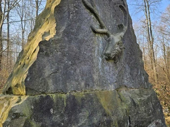 Bad-Driburg-Langeland_Bodostein.jpg Steinskulptur mit Hirschkopf in Waldumgebung am blauen Himmel.