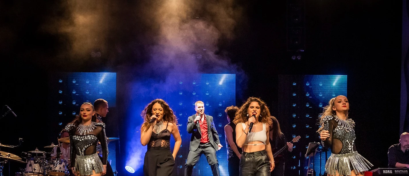 One Moment in Time_Whitney Houston Paderborn Fünf Künstler performen auf einer Bühne, darunter ein Mann im Anzug und vier Frauen mit Mikrofonen.