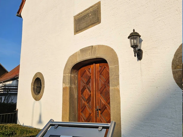 Der Eingang der St. Josef Kapelle mit einem Metallschild und zugehörigen QR-Code.