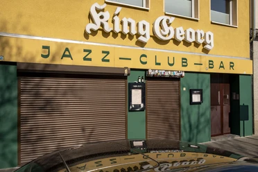 King Georg King Georg Jazzclub mit gelber Fassade und geschlossenen Rollläden, Köln bei Tageslicht.