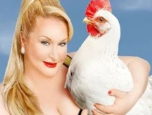 Eine lächelnde Person mit blonden Haaren hält ein weißes Huhn vor einem klaren blauen Himmel.