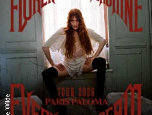 Musikerin Florence Welch von Florence + The Machine in einem weißen Kleid vor einem Fenster posierend.