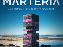 Stapel dunkler, mit rosa Schrift versehenen Blöcke spiegeln sich am Strand im ruhigen Wasser wider.