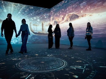 TUTANCHAMUN – Ein immersives Abenteuer Eine Gruppe von Menschen bewegt sich in einem dunklen Raum, umgeben von ägyptischen Lichtprojektionen.A group of people move around in a dark room, surrounded by Egyptian light projections.