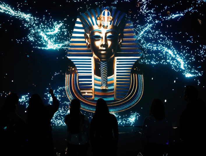 TUTANCHAMUN – Ein immersives Abenteuer Die beeindruckende Maske des Tutanchamun leuchtet eindrucksvoll vor dunklem Hintergrund.The impressive mask of Tutankhamun glows impressively against a dark background.